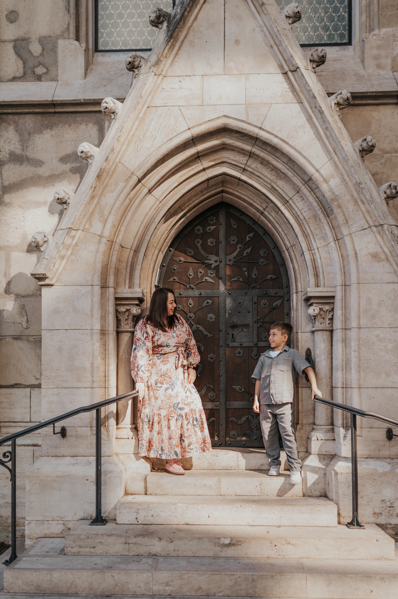 A mother and her nine-year-old son standing on the steps in front of a carved Gothic doorway during their family photoshoot in Budapest.