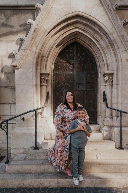 A portrait together by the Gothic doorway | Budapest family photoshoot A mother standing closely behind her son on stone steps beneath a pointed Gothic doorway during their family photoshoot in Budapest.