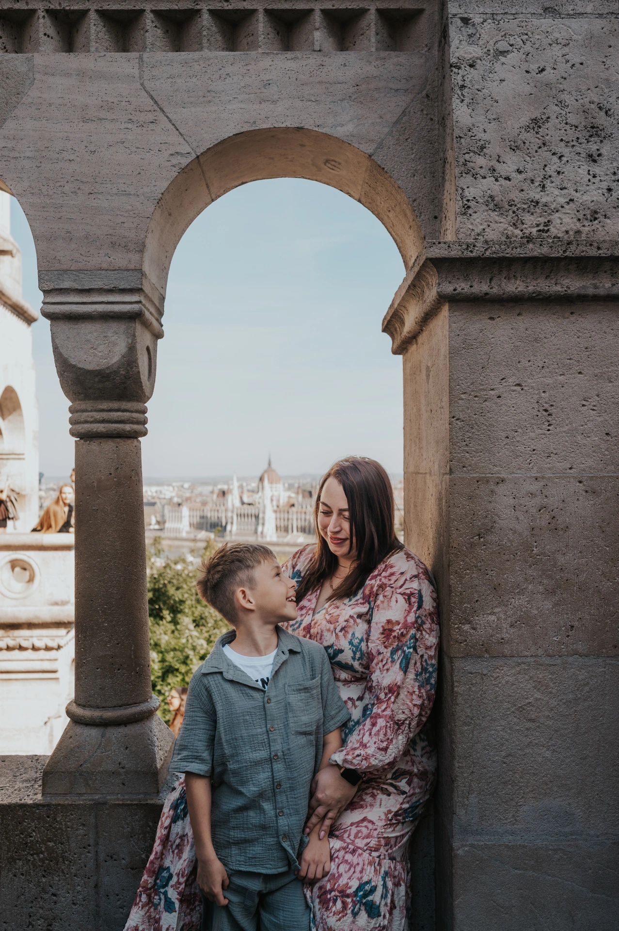 A closer portrait of a mother and son looking at one another beneath the pale stone arches of Fisherman’s Bastion during their family photoshoot in Budapest.