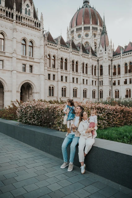 Budapest family photoshoot with a child lifted beside Parliament A parent lifting a child above the seated family during their Budapest family photoshoot, with Parliament’s dome and stonework behind them.