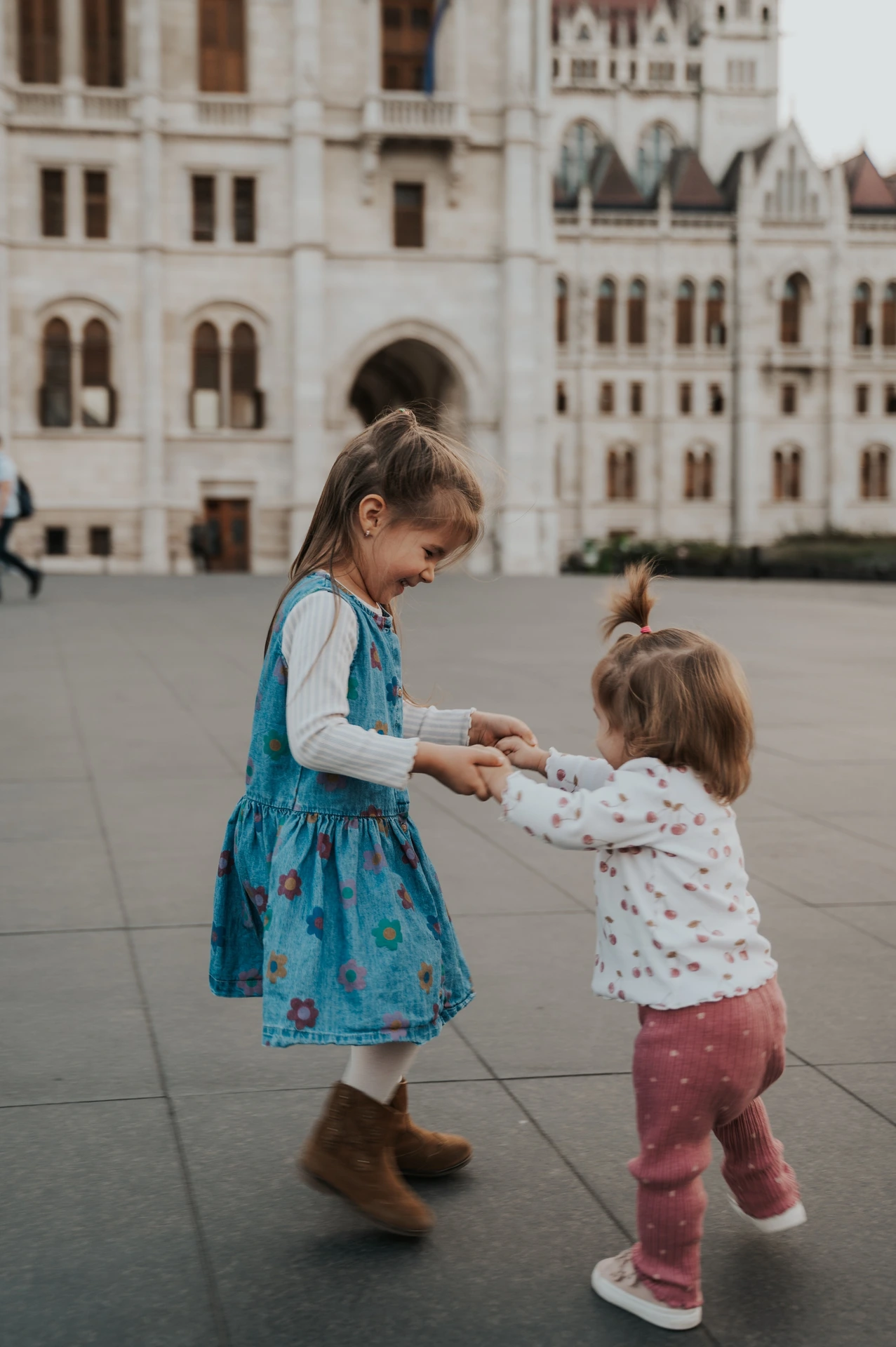 The two young children facing each other and holding hands during their Budapest family photoshoot, with Parliament’s pale stone façade behind them.