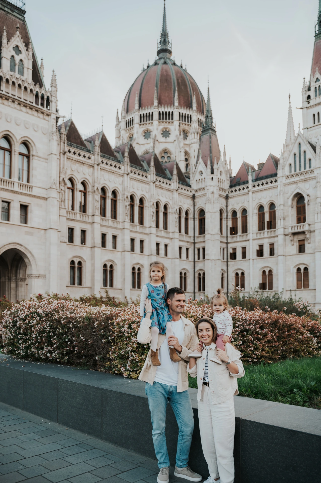 Family photoshoot in Budapest with the children on shoulders The family standing close together with the children on their parents’ shoulders during their Budapest family photoshoot beside Parliament.