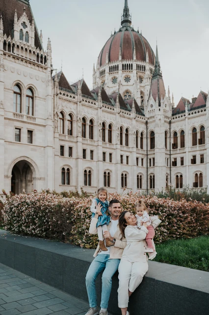 Family photoshoot in Budapest together on the Parliament ledge A closer view of the parents and two children together on the stone ledge during their Budapest family photoshoot in front of Parliament.