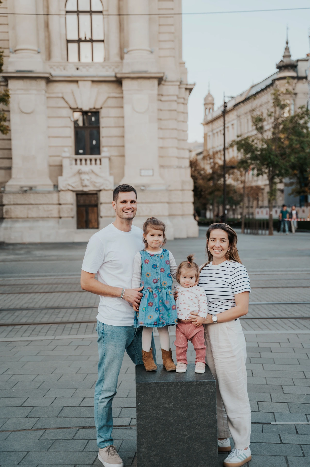 A closer portrait of the family during their Budapest family photoshoot, with both children standing between their parents on a low stone post.