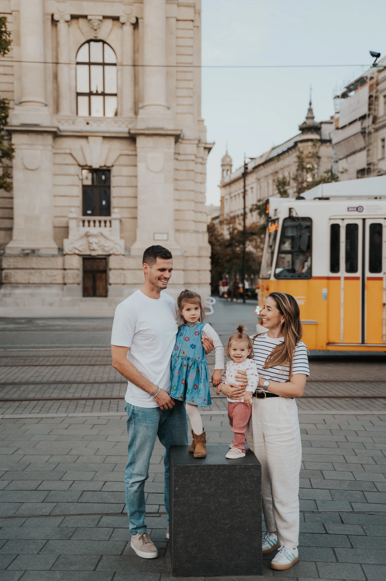 A closer view of the family standing together during their Budapest family photoshoot, with the children between their parents and a yellow tram behind them.