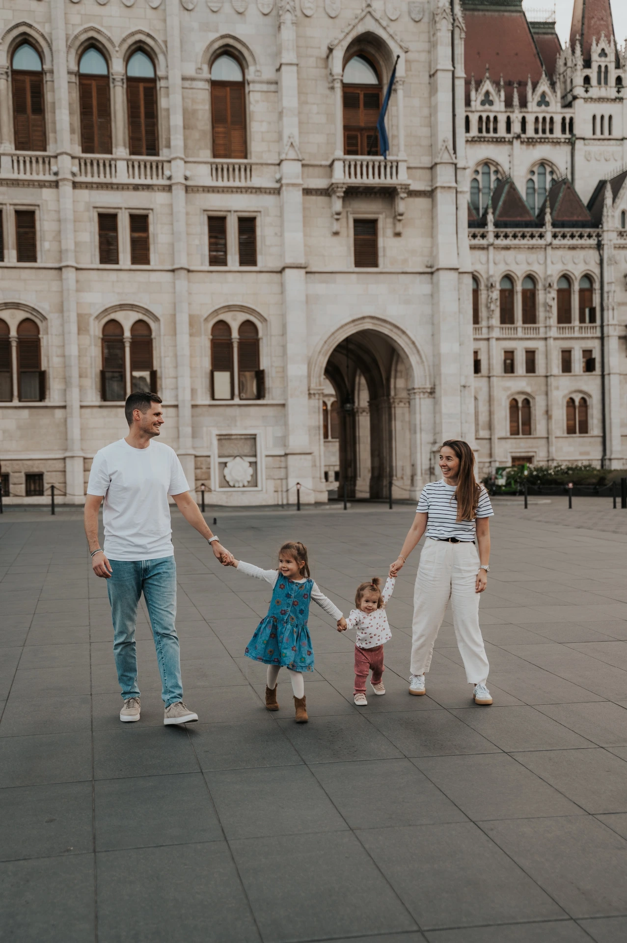 The parents guiding their children by the hand across the square during their Budapest family photoshoot near Parliament.