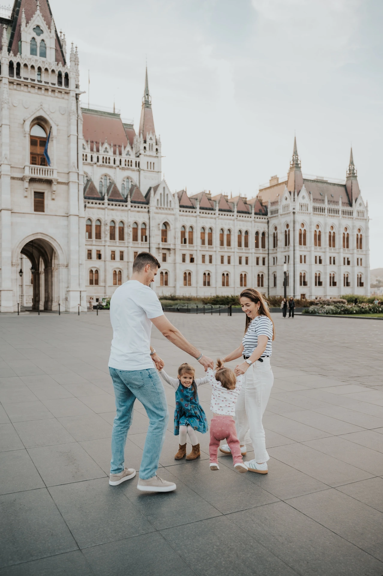 Family photoshoot in Budapest playing in a circle by Parliament The family linking hands in a small circle during their Budapest family photoshoot, with the wide paved square and Parliament around them.