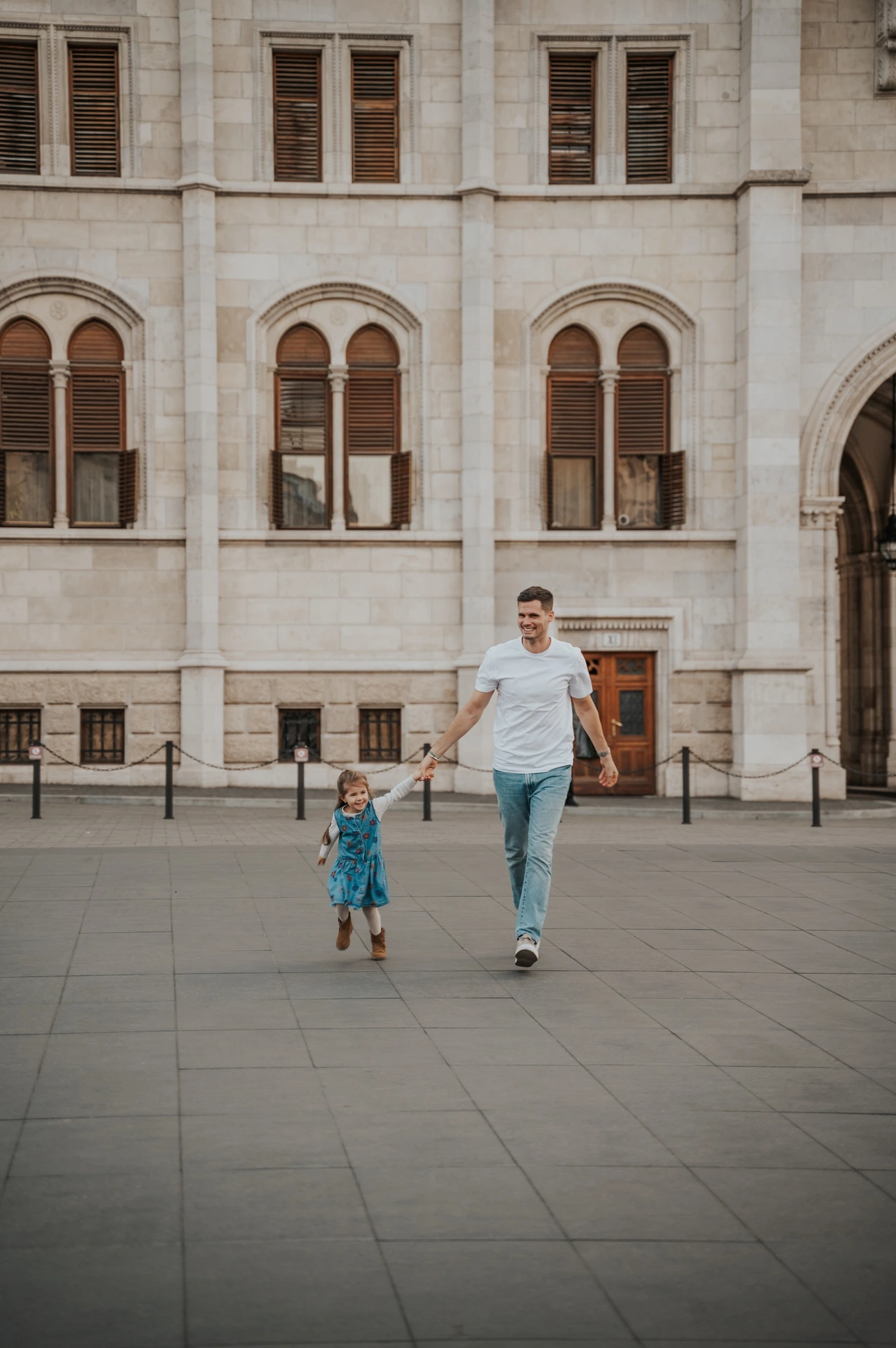 A parent walking hand in hand with a child during their Budapest family photoshoot, with Parliament’s stone windows and façade behind them.