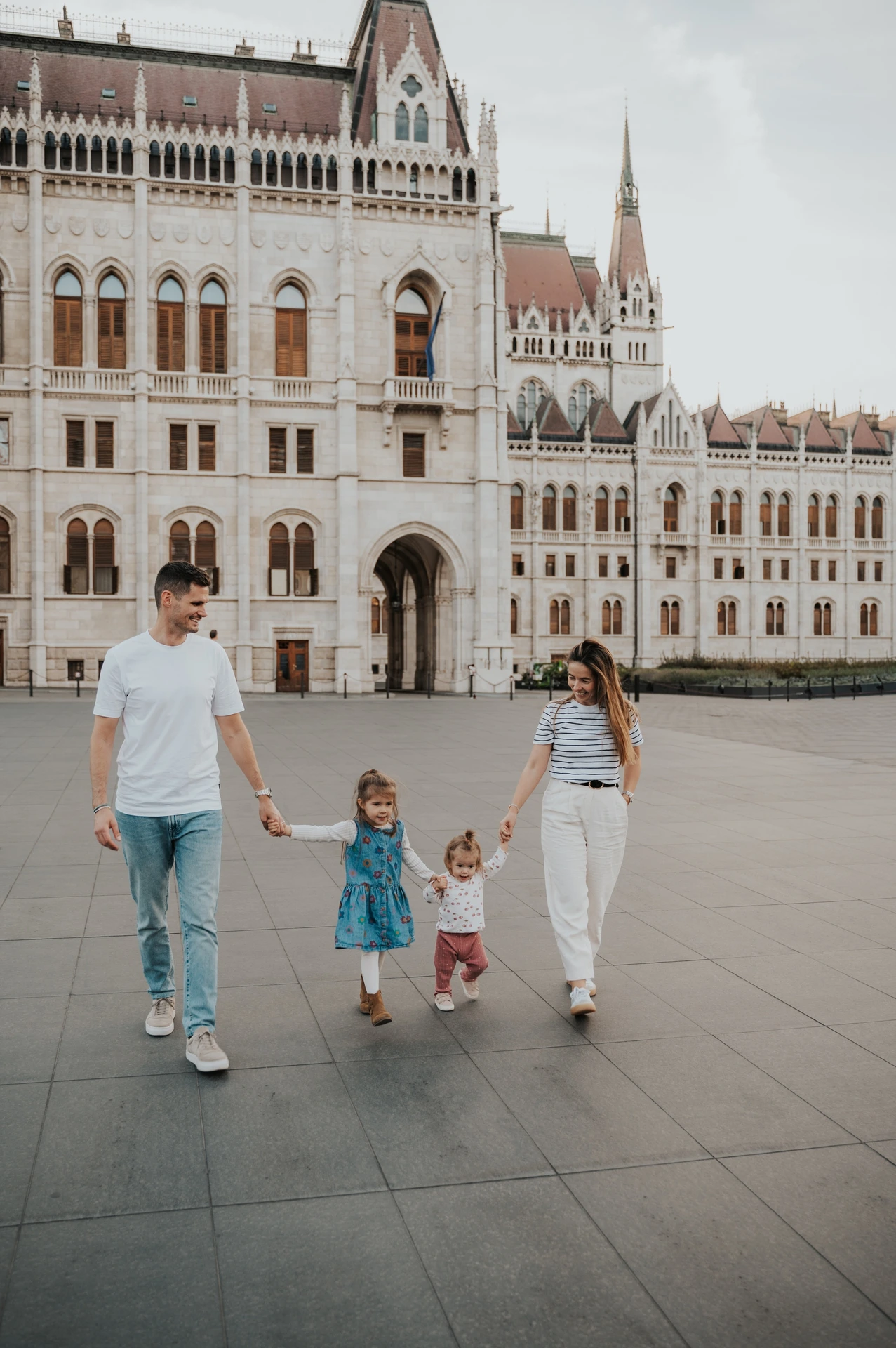 Budapest family photoshoot with the children between their parents The family walking towards the camera during their Budapest family photoshoot, with the children between their parents and Parliament behind them.