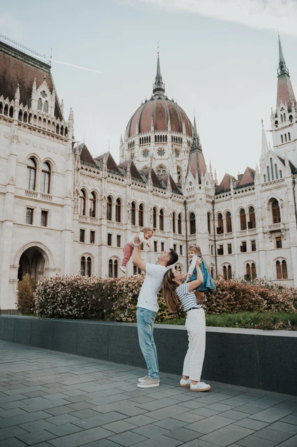 A wide view of the parents raising their children during their Budapest family photoshoot, with Parliament’s dome above the flowerbeds.