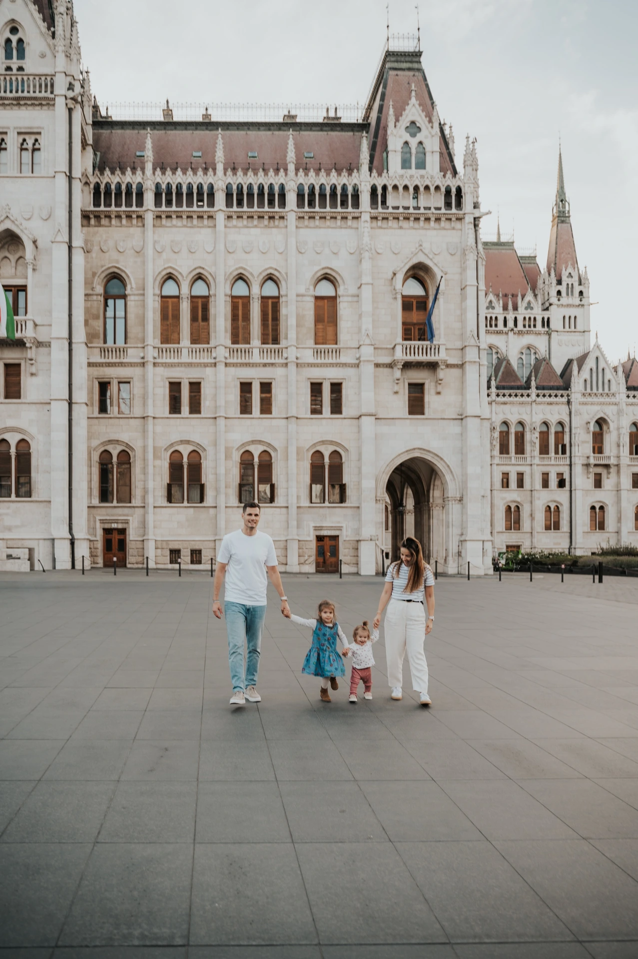 Budapest family photoshoot walking together across Parliament Square Wide view of the family walking hand in hand across the square during their Budapest family photoshoot, with the Hungarian Parliament filling the background.