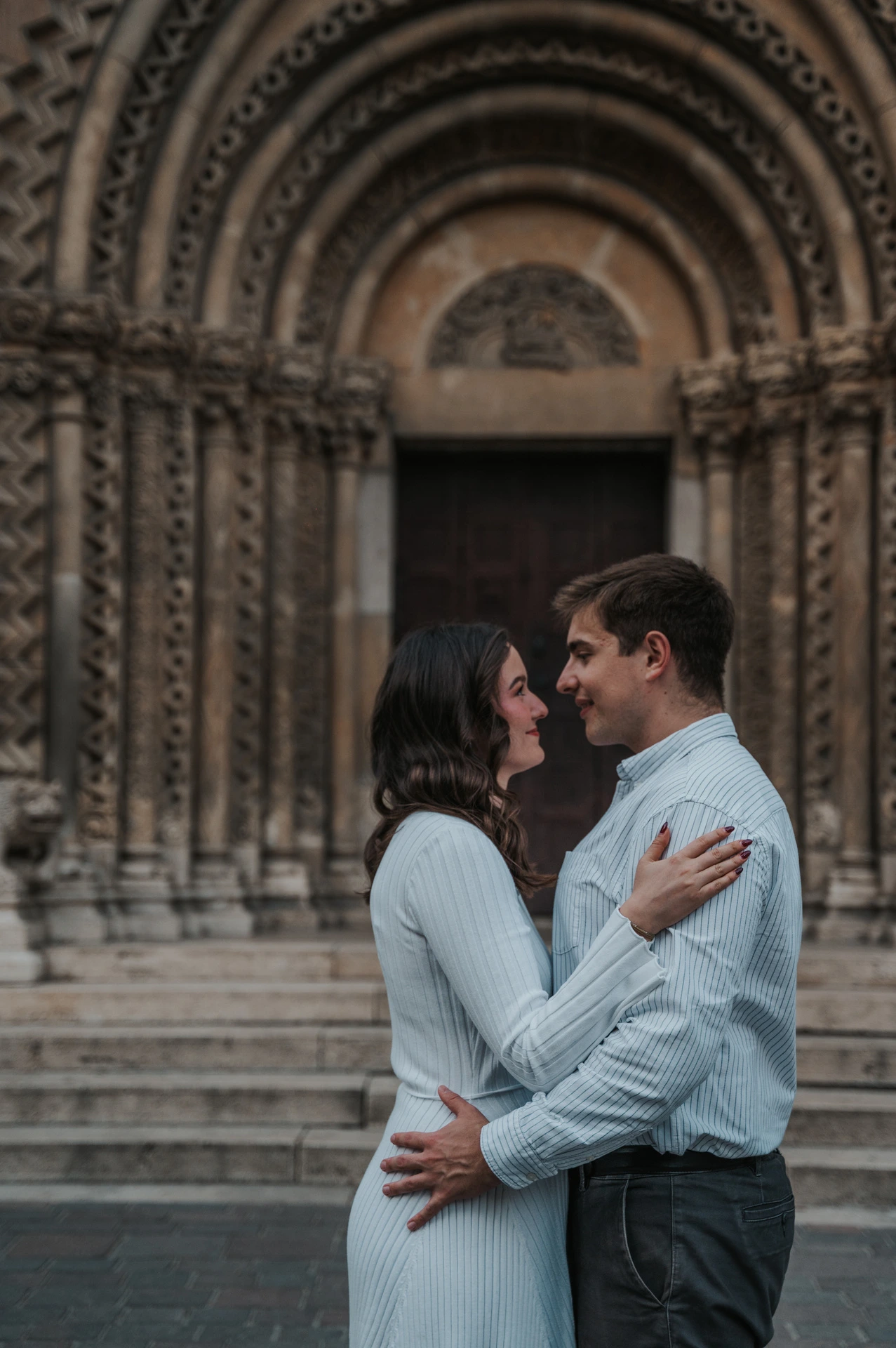 The couple embracing in front of the carved arched doorway at Vajdahunyad Castle during their anniversary photoshoot in Budapest.