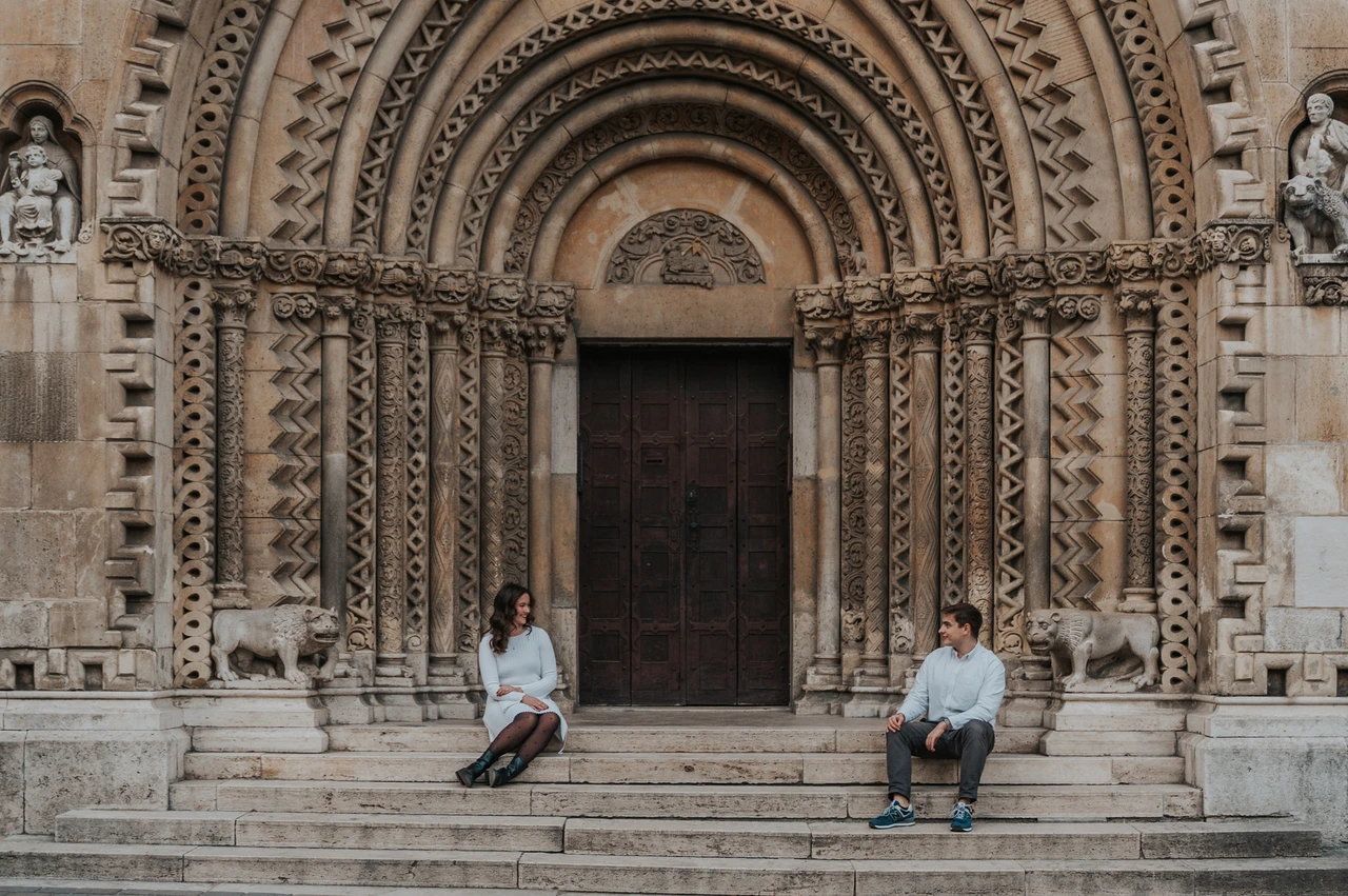A little time on the castle steps at a Budapest anniversary photoshoot A landscape portrait of the couple sitting apart on the stone steps beneath Vajdahunyad Castle’s carved doorway during their anniversary photoshoot in Budapest.