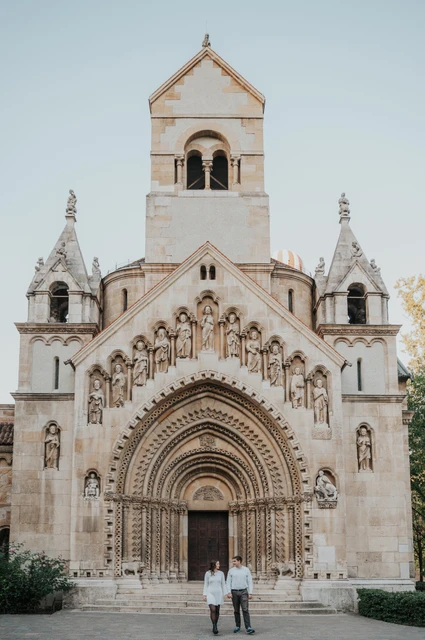 The couple standing in front of the tall chapel façade and carved doorway at Vajdahunyad Castle during their anniversary photoshoot in Budapest.