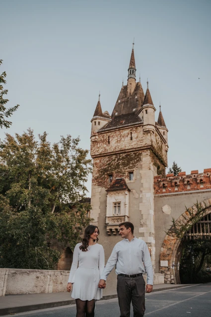 The couple walking hand in hand beneath Vajdahunyad Castle’s pointed entrance tower during their anniversary photoshoot in Budapest.
