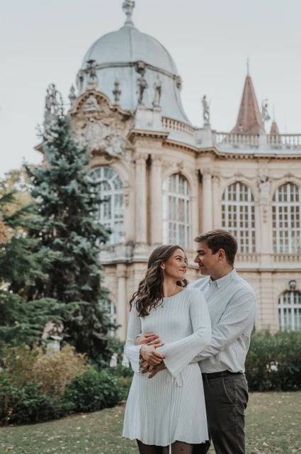 A close embrace in the castle gardens at a Budapest anniversary photoshoot A closer portrait of the couple embracing with Vajdahunyad Castle’s pale palace façade in the background during their anniversary photoshoot in Budapest.