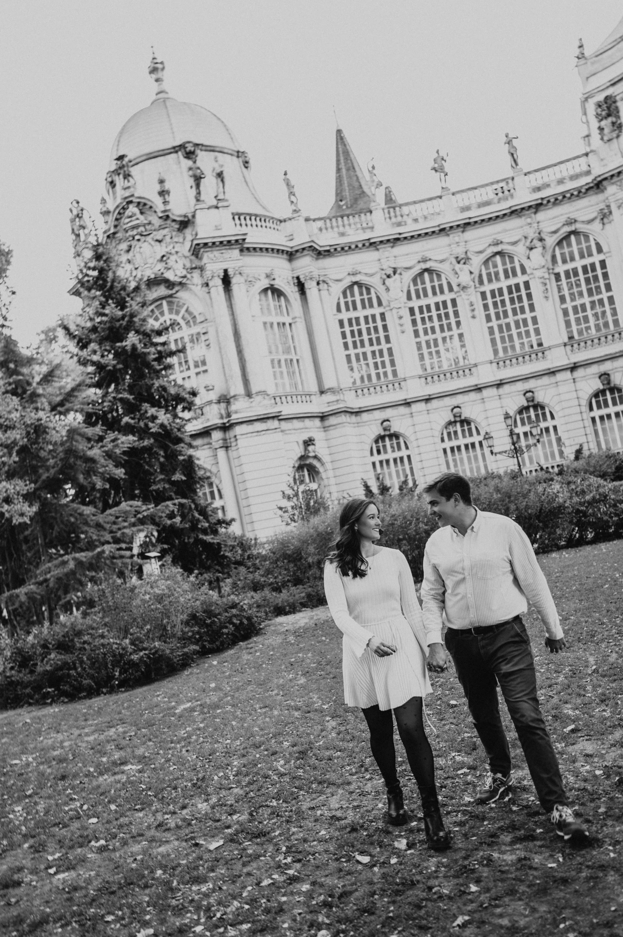 Black-and-white portrait of the couple holding hands on the grass in front of Vajdahunyad Castle’s ornate palace façade during their anniversary photoshoot in Budapest.