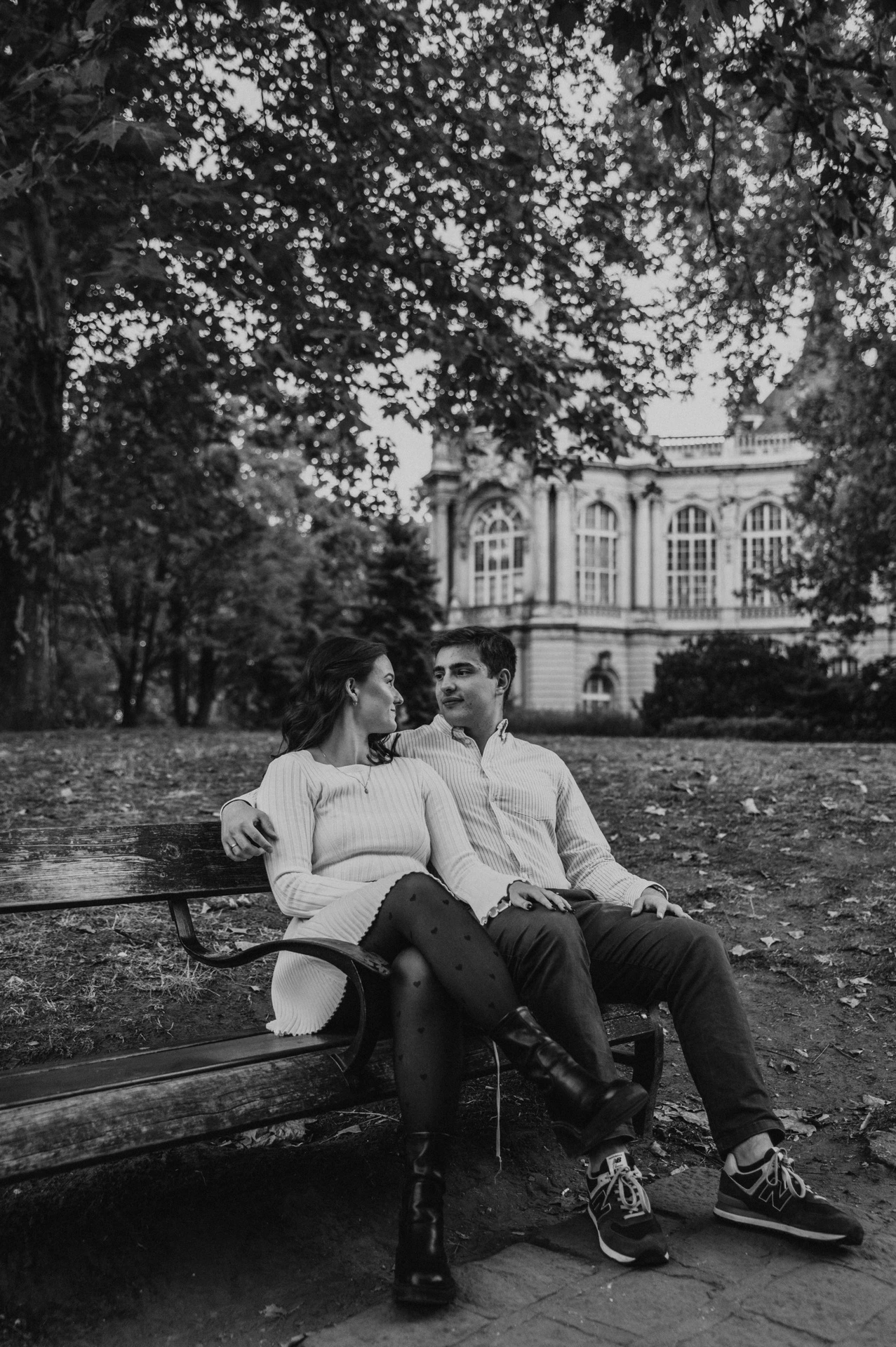 Black-and-white portrait of the couple sitting together on a wooden bench near Vajdahunyad Castle during their anniversary photoshoot in Budapest.