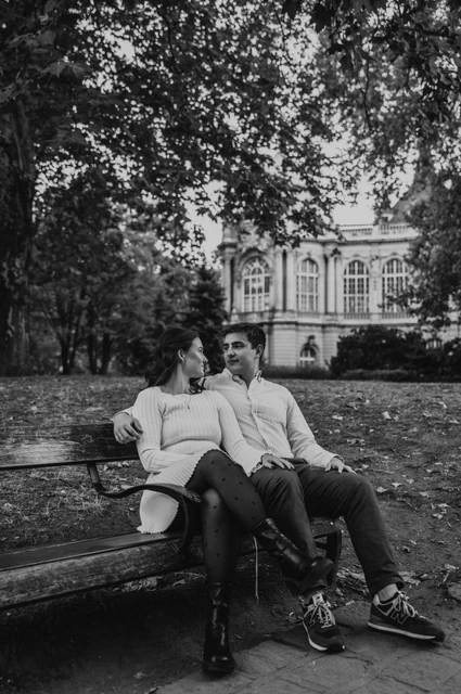 A bench portrait in black and white at a Budapest anniversary photoshoot Black-and-white portrait of the couple sitting together on a wooden bench near Vajdahunyad Castle during their anniversary photoshoot in Budapest.