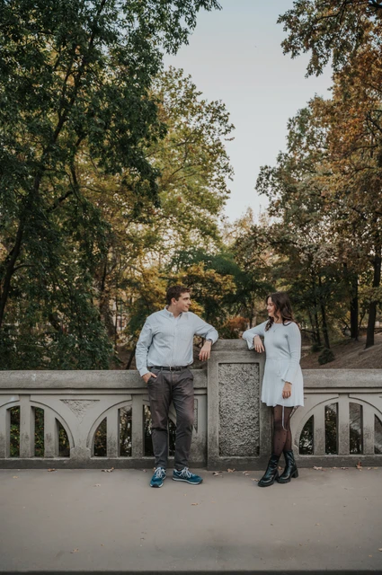 A leafy corner by the stone bridge at a Budapest anniversary photoshoot The couple leaning beside a stone bridge railing beneath leafy trees near Vajdahunyad Castle during their anniversary photoshoot in Budapest.