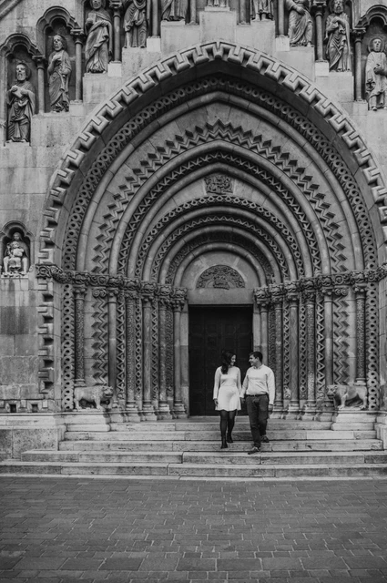 A walk down the castle steps in black and white at a Budapest anniversary photoshoot Black-and-white portrait of the couple walking down the steps beneath Vajdahunyad Castle’s ornate doorway during their anniversary photoshoot in Budapest.