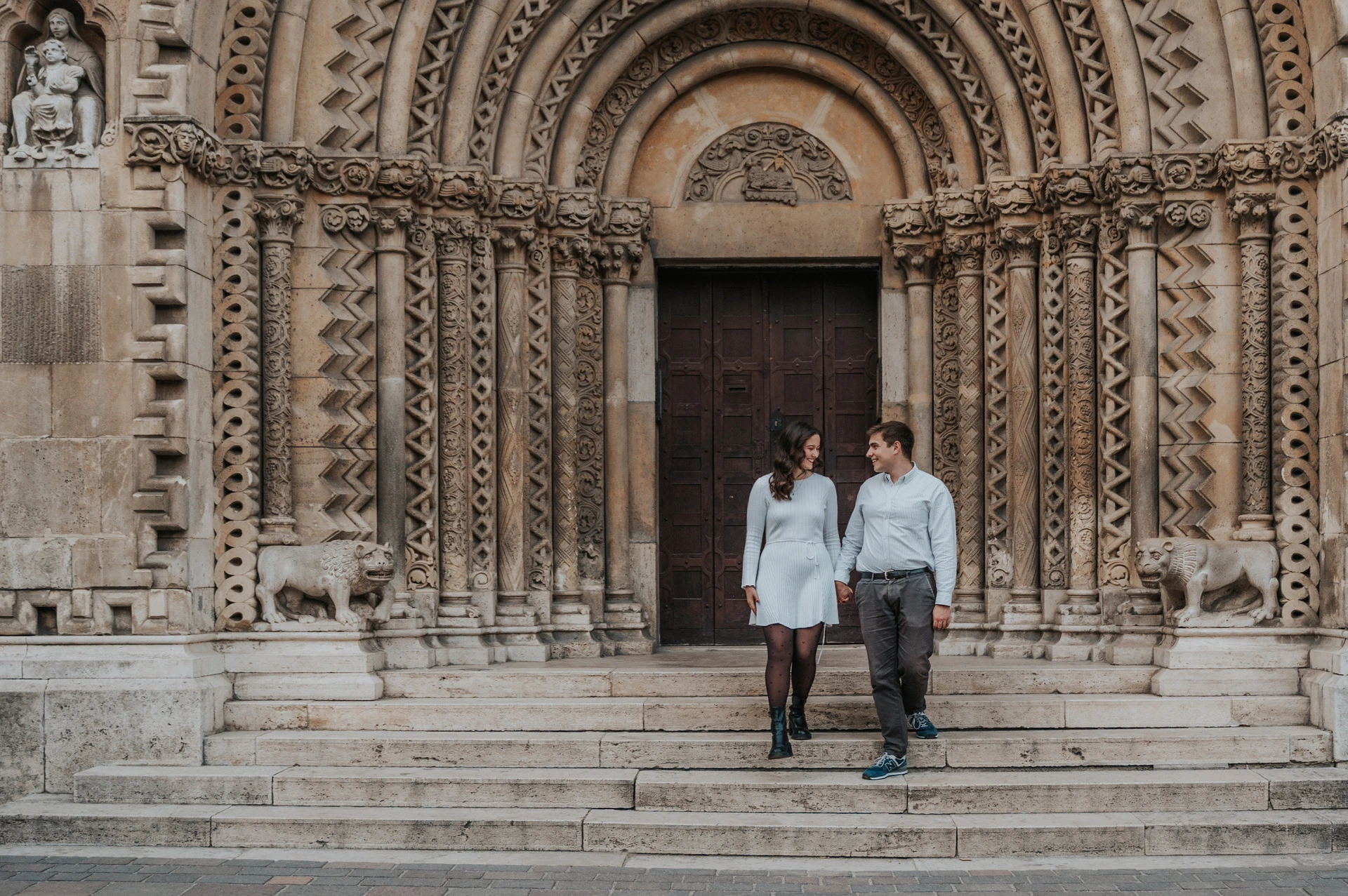 Walking down the beautiful castle steps at a Budapest anniversary photoshoot A wide portrait of the couple walking down the stone steps beneath Vajdahunyad Castle’s carved arches during their anniversary photoshoot in Budapest.