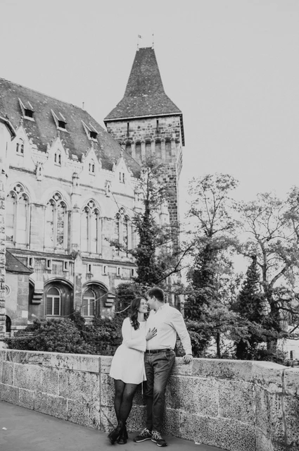 The castle tower in black and white at a Budapest anniversary photoshoot Black-and-white portrait of the couple leaning close beside a stone wall beneath Vajdahunyad Castle’s tower during their anniversary photoshoot in Budapest.