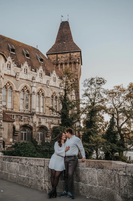 A romantic corner beneath the castle tower at a Budapest anniversary photoshoot The couple leaning towards one another beside a stone wall beneath Vajdahunyad Castle’s tall tower during their anniversary photoshoot in Budapest.