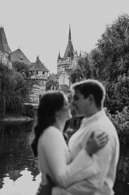 A soft waterside portrait in black and white at a Budapest anniversary photoshoot A softly focused black-and-white portrait of the couple leaning close beside the water with Vajdahunyad Castle behind them during their anniversary photoshoot in Budapest.