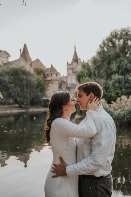 A kiss beside the water and castle at a Budapest anniversary photoshoot The couple leaning close for a kiss beside the water with Vajdahunyad Castle’s turrets and reflection behind them during their anniversary photoshoot in Budapest.