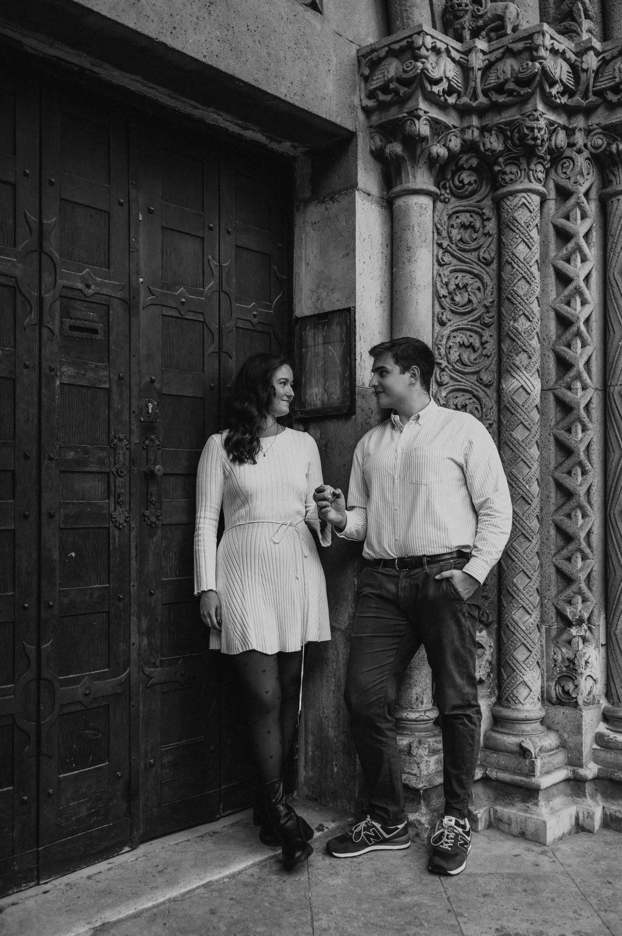 Black-and-white portrait of the couple standing together beside a dark wooden door and carved stone column at Vajdahunyad Castle during their anniversary photoshoot in Budapest.
