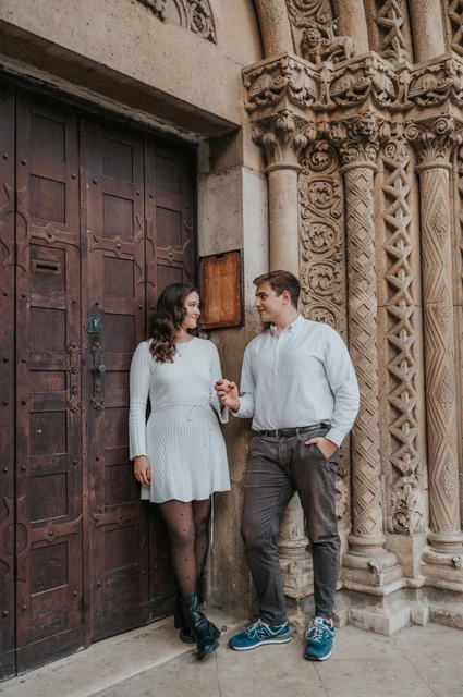 Smiles beside the carved stone doorway at a Budapest anniversary photoshoot The couple smiling at one another beside a dark wooden door and carved stone column at Vajdahunyad Castle during their anniversary photoshoot in Budapest.