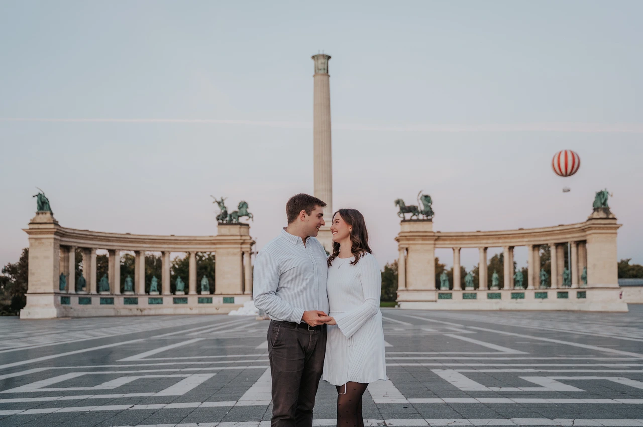 Anniversary smiles at Heroes’ Square at a Budapest anniversary photoshoot A landscape portrait of the couple smiling at one another at Heroes’ Square with its central column and colonnade behind them during their anniversary photoshoot in Budapest.