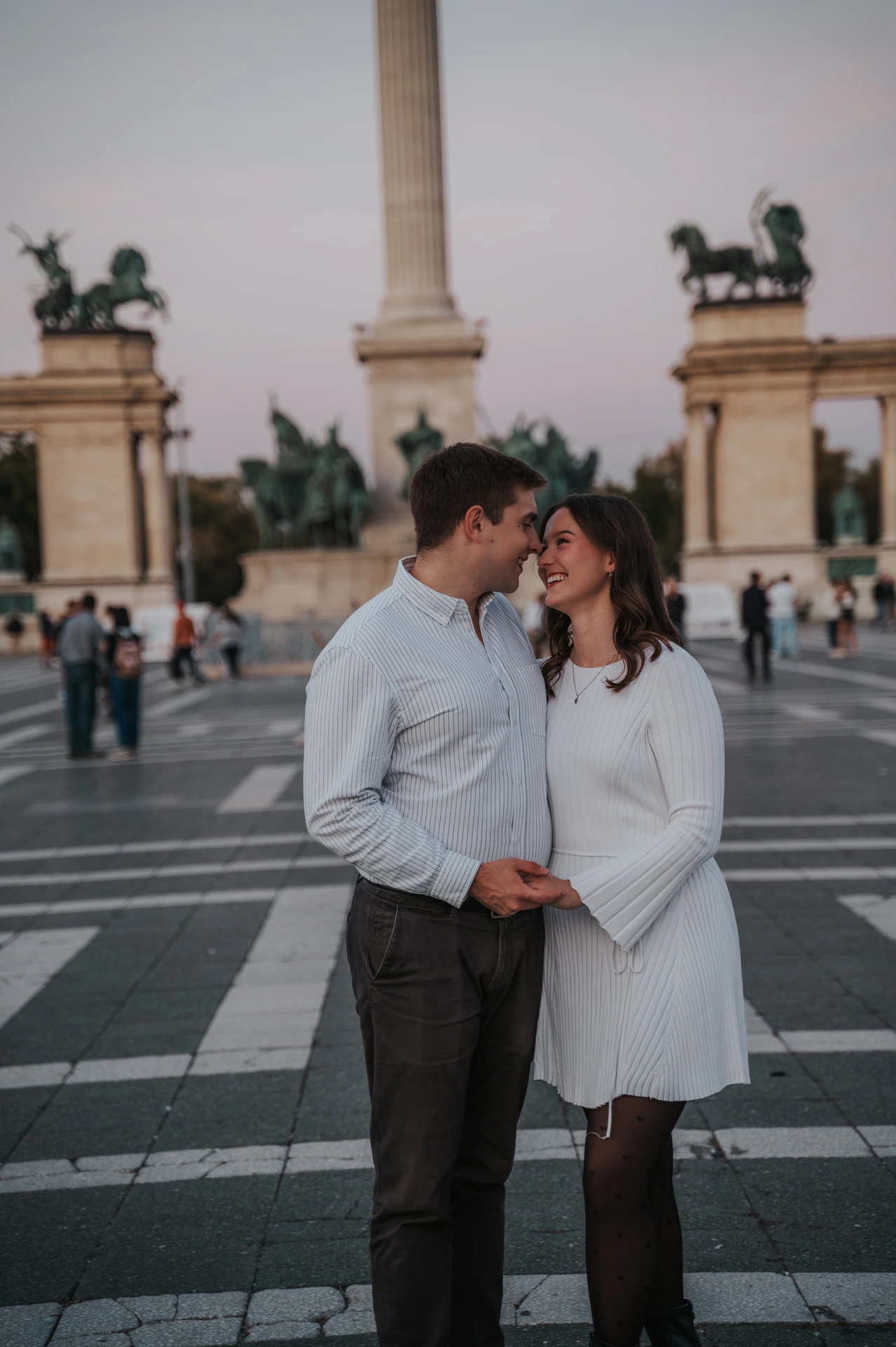 The couple leaning close together in front of the central column at Heroes’ Square during their anniversary photoshoot in Budapest.