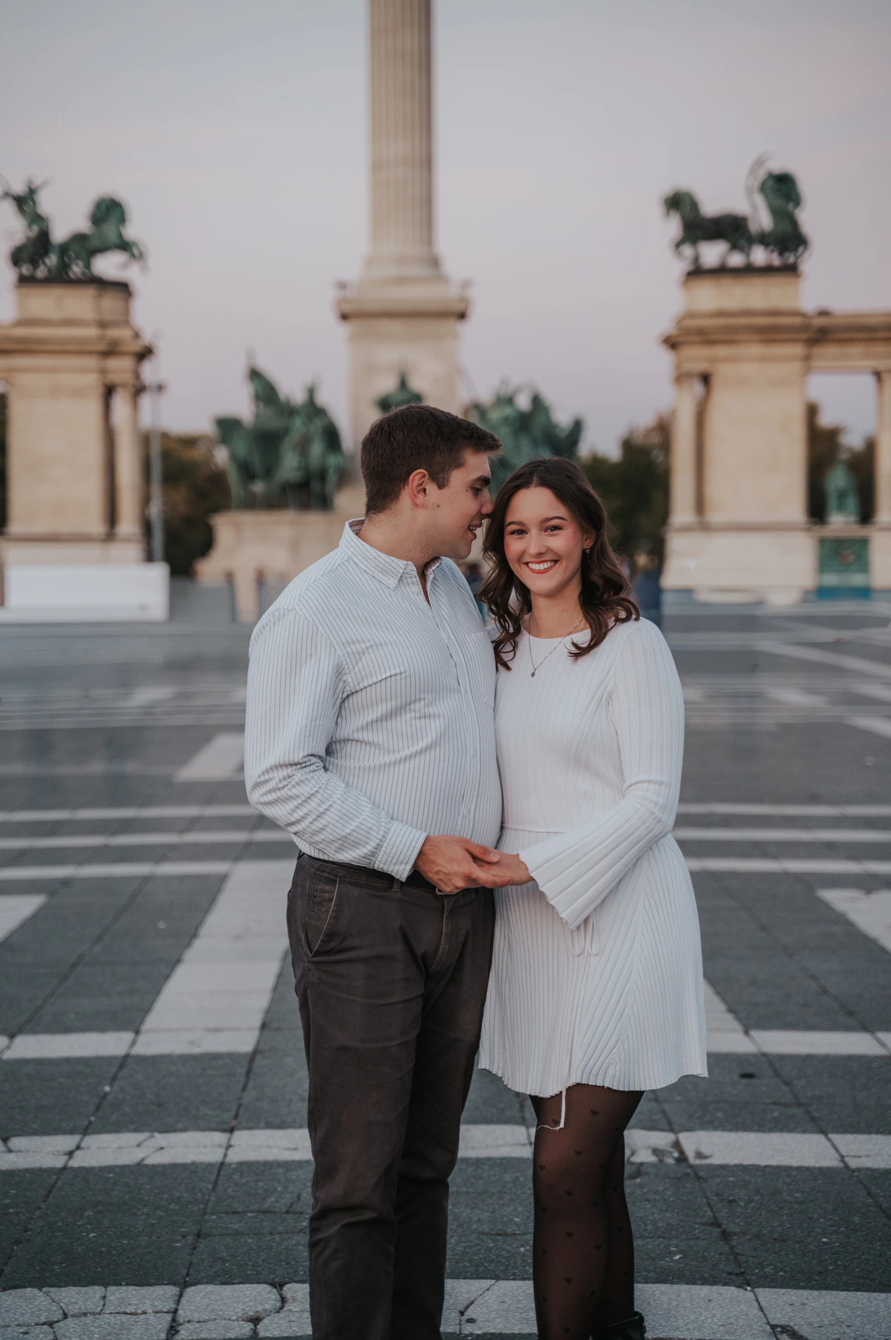 A close portrait of the man kissing his smiling partner near her temple at Heroes’ Square during their anniversary photoshoot in Budapest.
