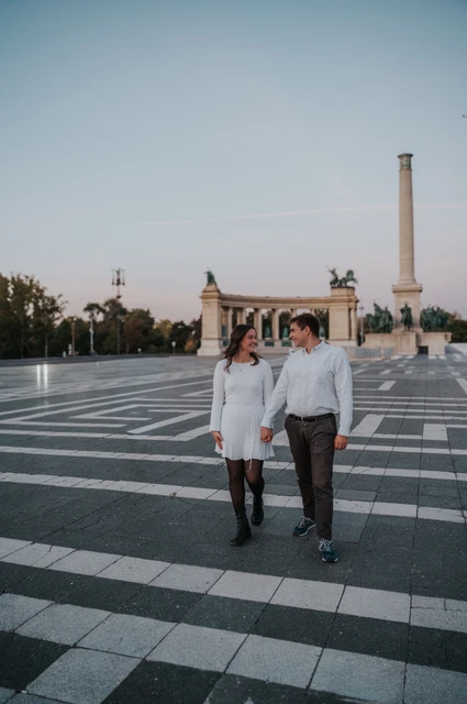 Walking together at Heroes’ Square at a Budapest anniversary photoshoot The couple walking hand in hand across Heroes’ Square beneath a blue sky during their anniversary photoshoot in Budapest.