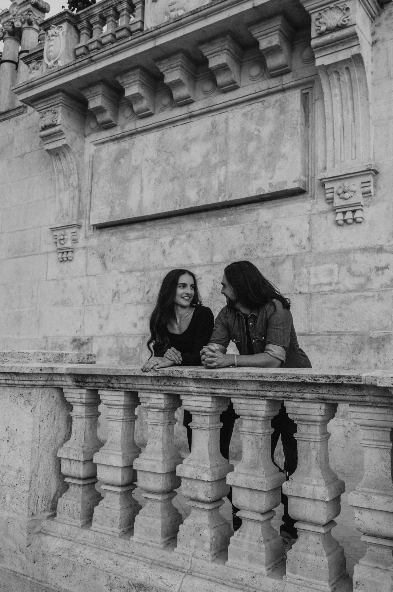 Black-and-white portrait of the couple leaning together on a stone balustrade at Buda Castle during their couple photoshoot in Budapest.