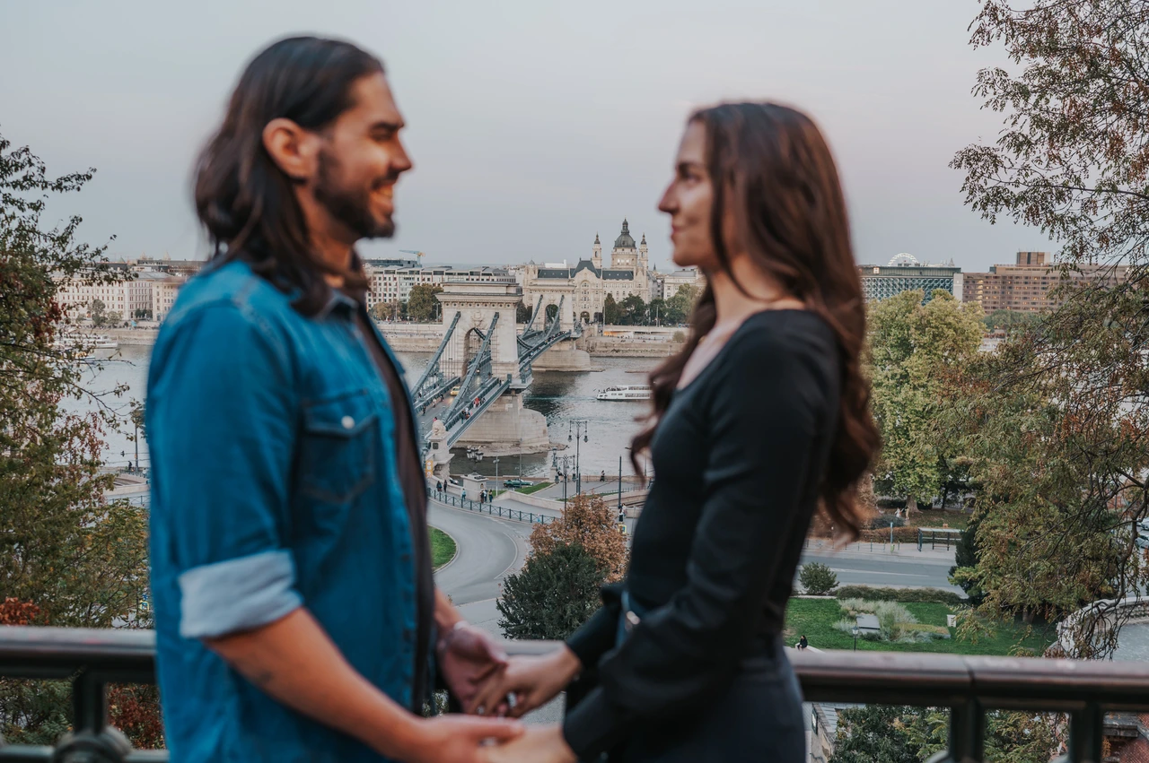 A city view framed by the couple at a Budapest couple photoshoot The couple holding hands in the softly focused foreground with the Chain Bridge and Budapest skyline in focus behind them during their couple photoshoot in Budapest.