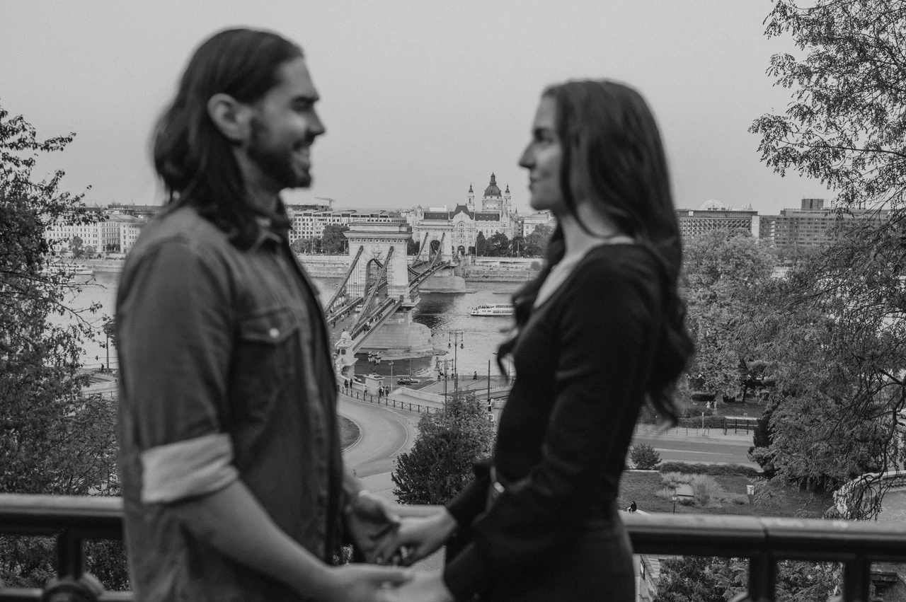 A wide city portrait in black and white at a Budapest couple photoshoot Black-and-white landscape portrait of the couple holding hands with the Chain Bridge and Budapest skyline behind them during their couple photoshoot in Budapest.