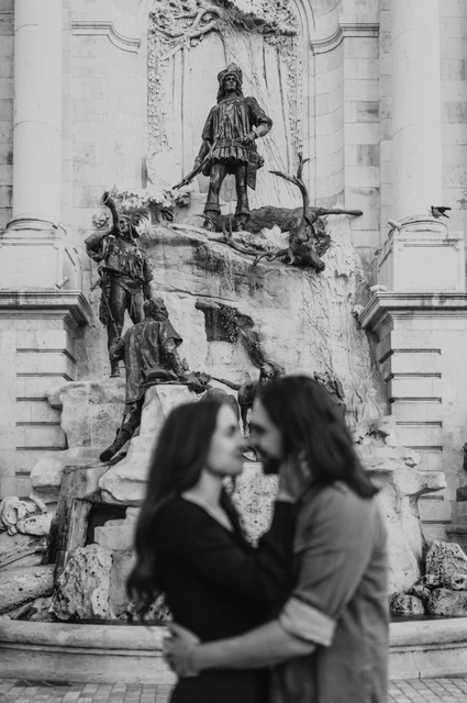 The castle fountain in black and white at a Budapest couple photoshoot Black-and-white portrait of the couple embracing in front of the bronze figures at Buda Castle’s fountain during their couple photoshoot in Budapest.