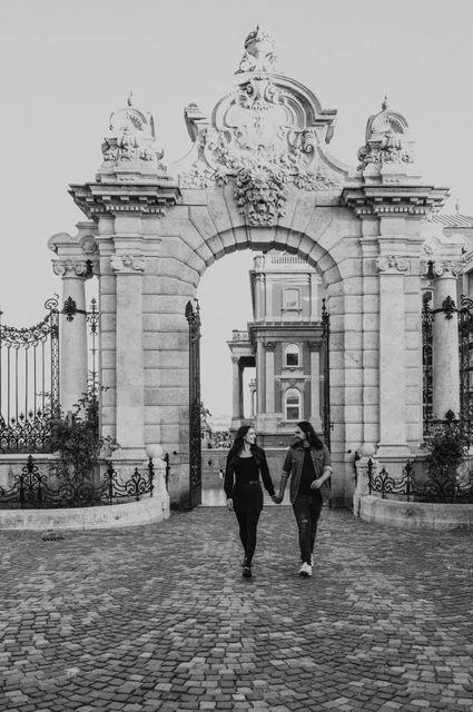 The castle gateway in black and white at a Budapest couple photoshoot Black-and-white portrait of the couple walking through an ornate stone gateway at Buda Castle during their couple photoshoot in Budapest.