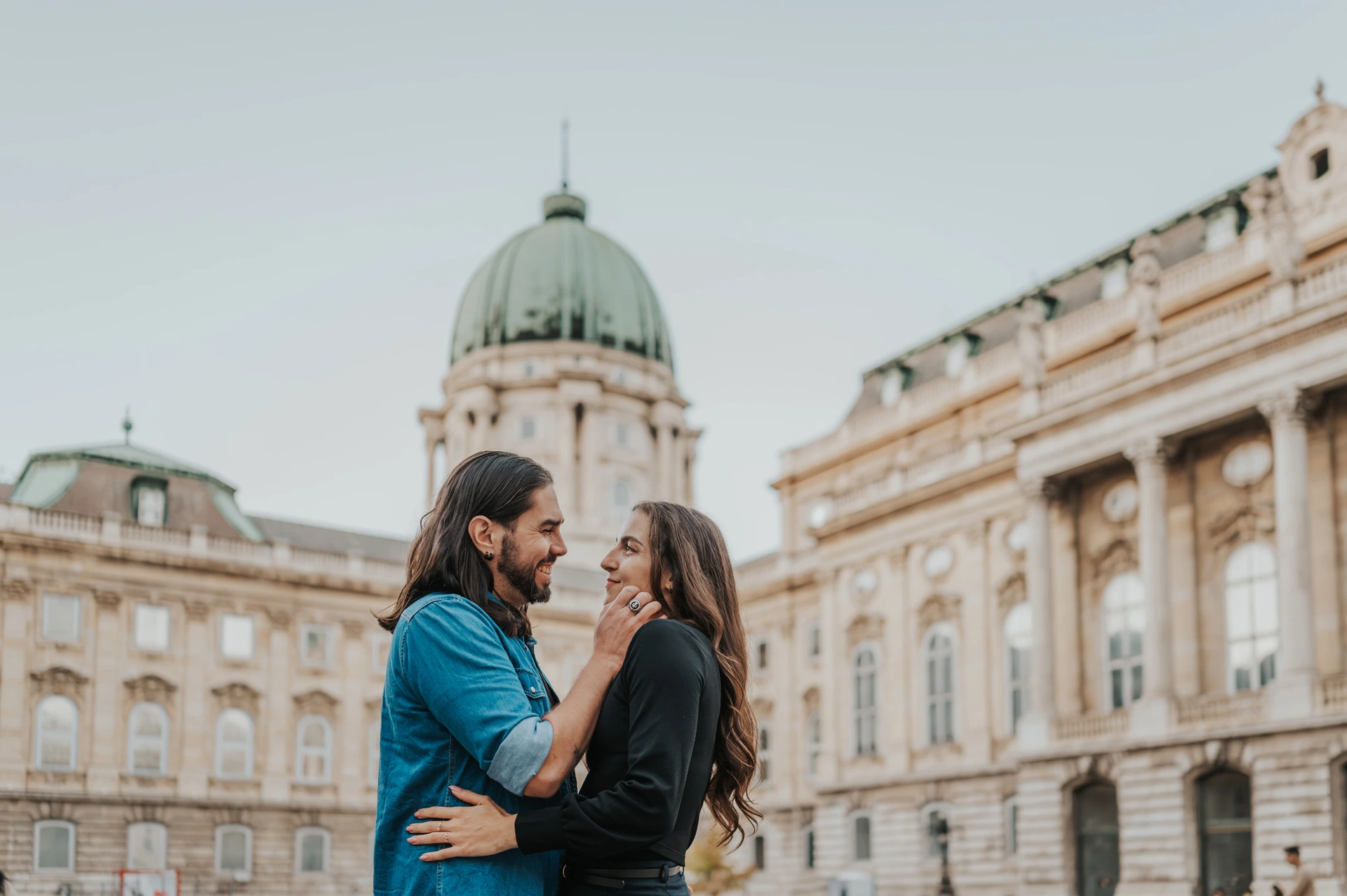 Smiles beneath Buda Castle’s green dome at a Budapest couple photoshoot A landscape portrait of the smiling couple embracing beneath Buda Castle’s green dome and pale palace façade during their couple photoshoot in Budapest.