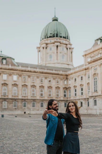 The couple sharing a playful portrait with outstretched arms beneath Buda Castle’s green dome during their couple photoshoot in Budapest.