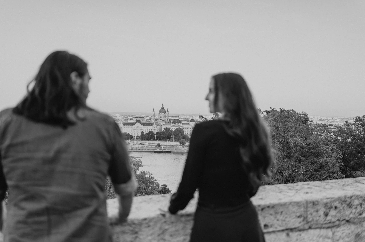 A Danube view in black and white at a Budapest couple photoshoot Black-and-white portrait of the couple seen from behind looking across the Danube from Buda Castle during their couple photoshoot in Budapest.