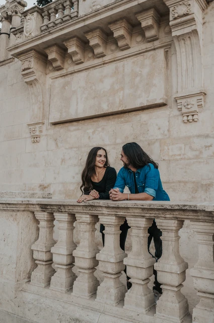 A little time by the stone balustrade at a Budapest couple photoshoot The couple leaning together on a stone balustrade beneath Buda Castle’s pale stone walls during their couple photoshoot in Budapest.