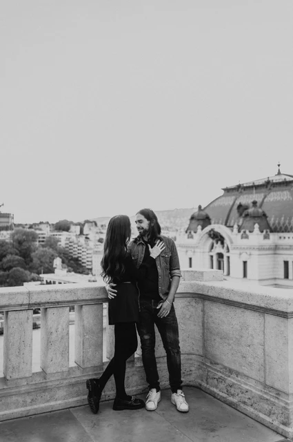 A castle terrace embrace in black and white at a Budapest couple photoshoot Black-and-white portrait of the couple embracing beside a stone terrace railing at Buda Castle during their couple photoshoot in Budapest.