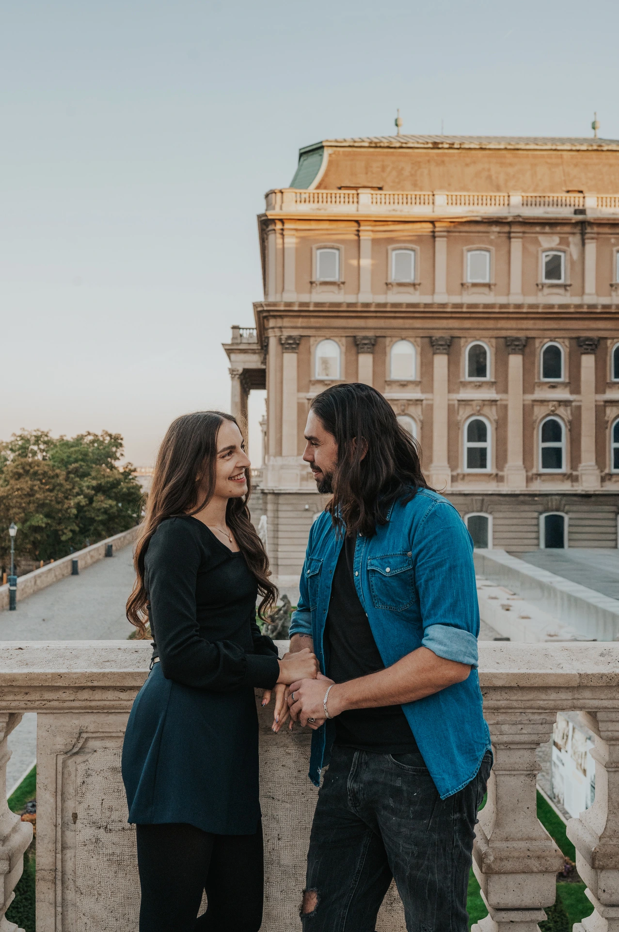 A close portrait of the couple holding hands on a terrace with Buda Castle’s palace façade behind them during their couple photoshoot in Budapest.