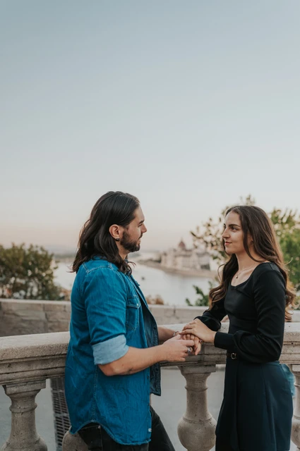 Holding hands above Budapest’s rooftops at a Budapest couple photoshoot The couple holding hands on a stone terrace at Buda Castle with Budapest’s rooftops beyond them during their couple photoshoot in Budapest.