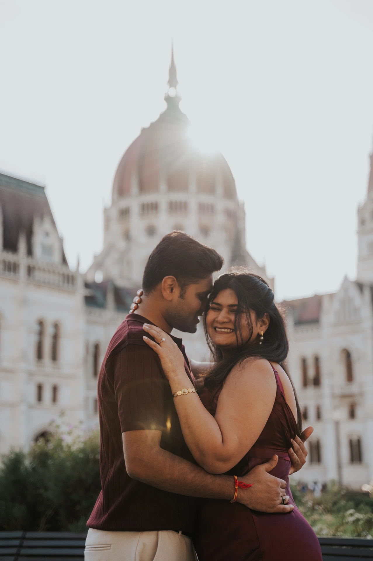 The couple smiling together in soft backlight with Parliament’s dome behind them during their Budapest couple photoshoot.