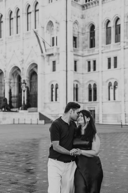A Budapest couple photoshoot by Parliament in black and white Black-and-white portrait of the couple touching foreheads beside Parliament’s arched façade during their couple photoshoot in Budapest.